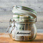 Dollar bills in glass jar isolated on wooden background. Saving money for retirement.